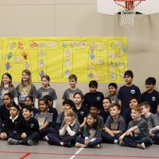 Class of students sitting and kneeling with their teacher in front of sign that reads "You Matter"