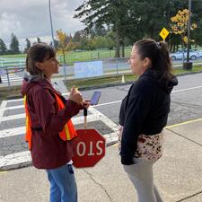 Two adults talking outside, one is holding stop sign.