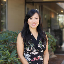 Women stands outside in front of building with greenery in the background