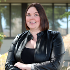 Woman with short brown hair wearing black leather jacket poses for photo